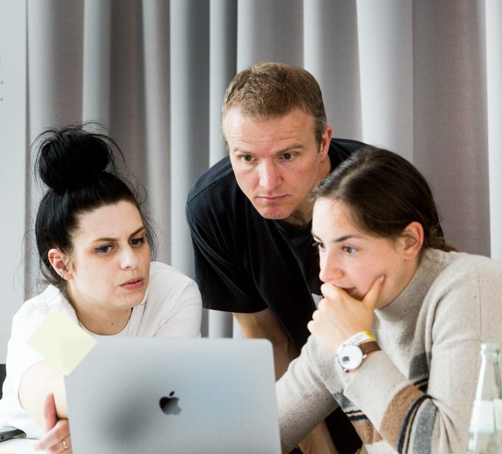 Auf dem Foto schauen Drei Koleg:innen nachdenklich auf den Bildschirm eines Laptops.